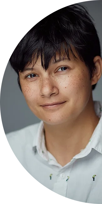 Pk Kulasegram a mixed-race person with tanned skin and short black hair, smiles at the camera. They are wearing a white shirt.